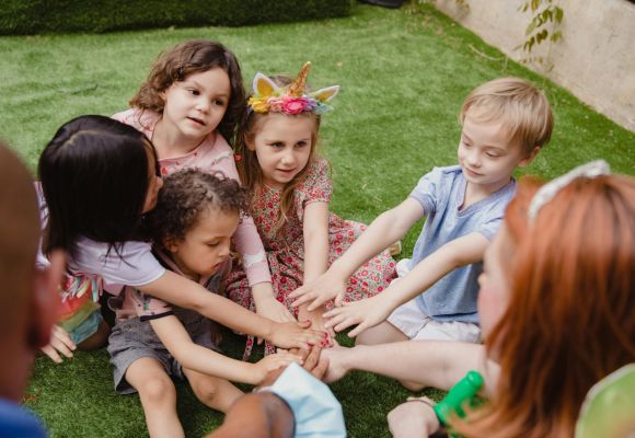 Kinder Im Kreis sitzend legen Hände in der Mitte zusammen