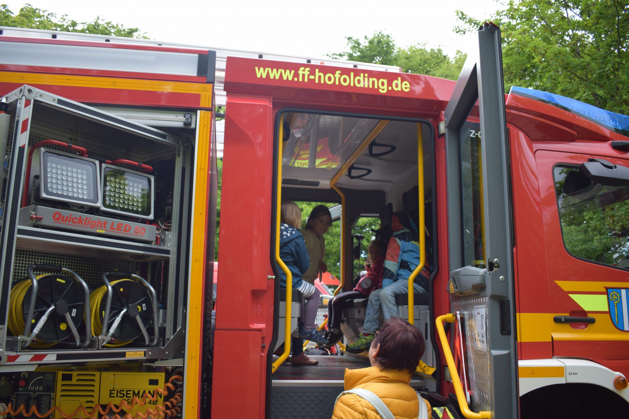 Kinder an Feuerwehrfahrzeug mit geöffneter Tür, manche drinnen