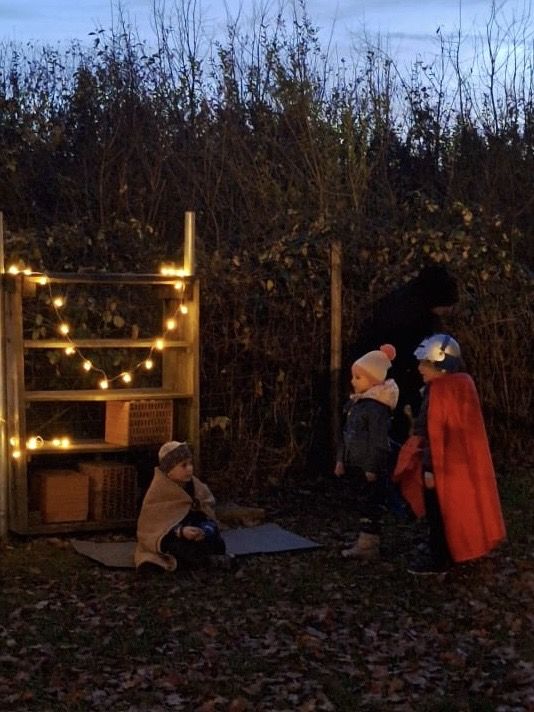 Kinder im dunklen Garten vor Regal mit Lichterkette