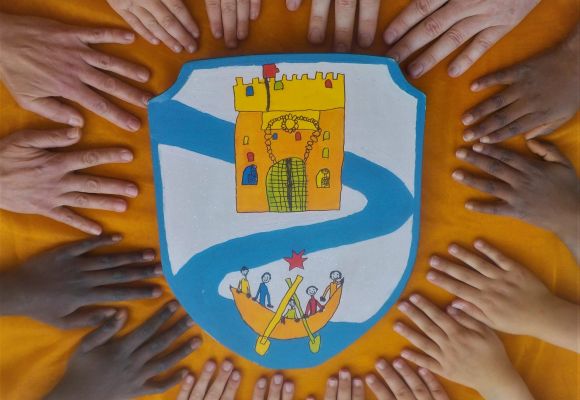 Kinderhände umrahmen eine Kinderzeichnung in Form eines Wappens mit der Burg Isaria und einem Schiff mit Menschen