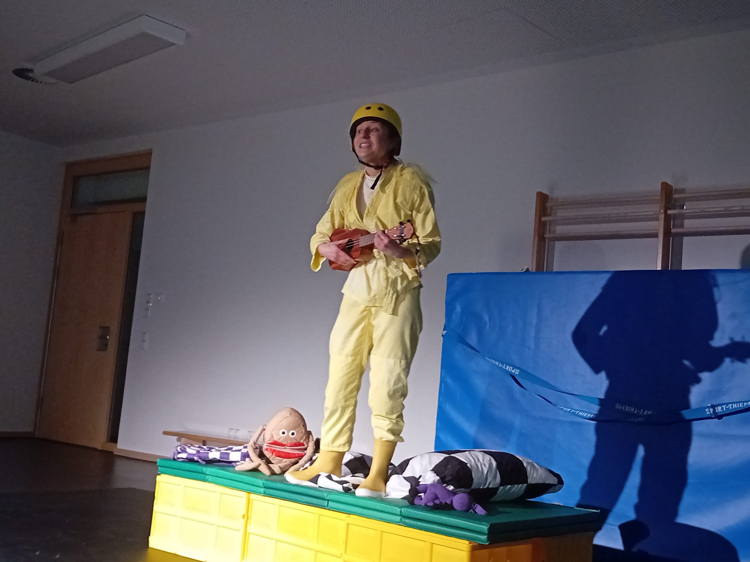 Theaterszene: Frau mit Fahrradhelm und kleiner Gitarre