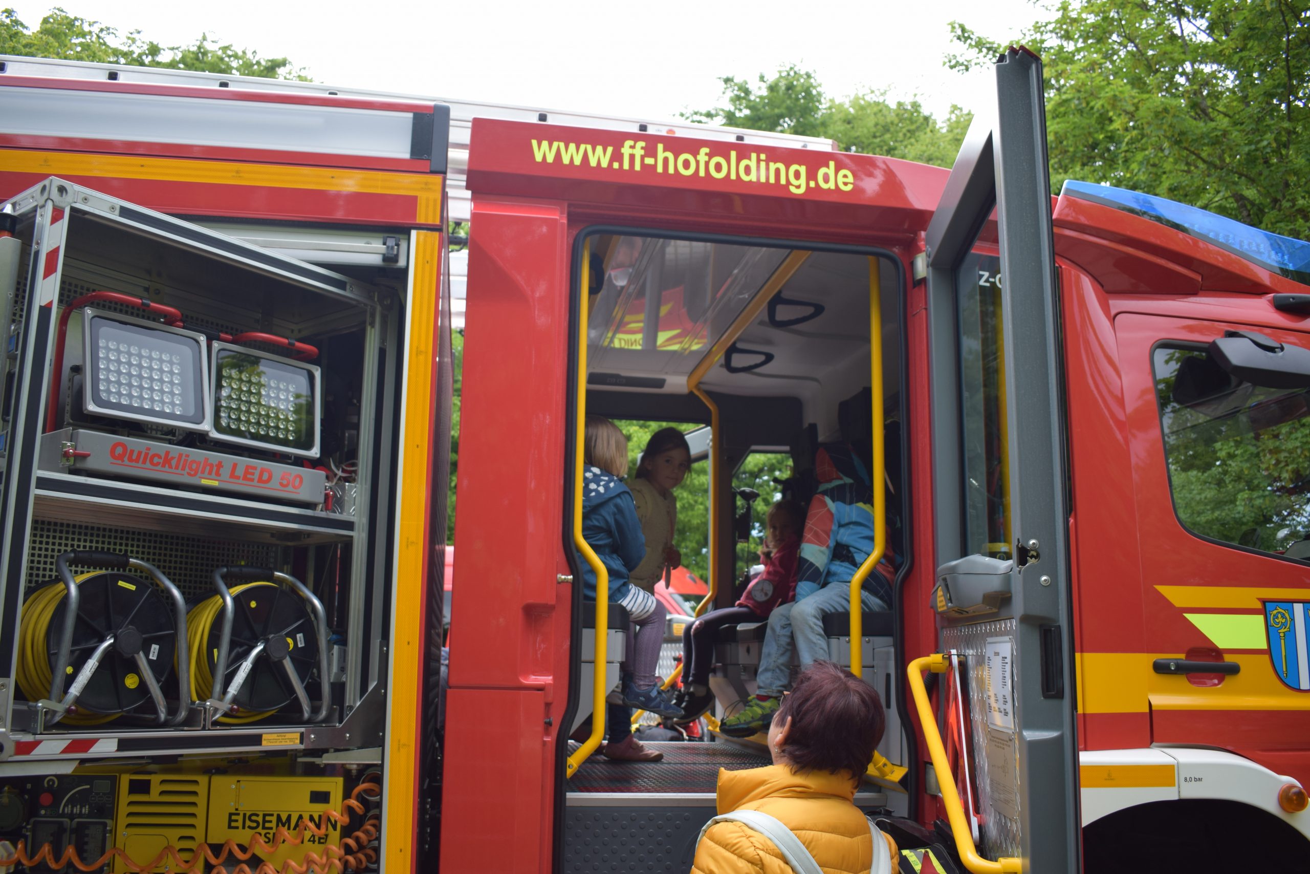 Kinder an Feuerwehrfahrzeug mit geöffneter Tür, manche drinnen