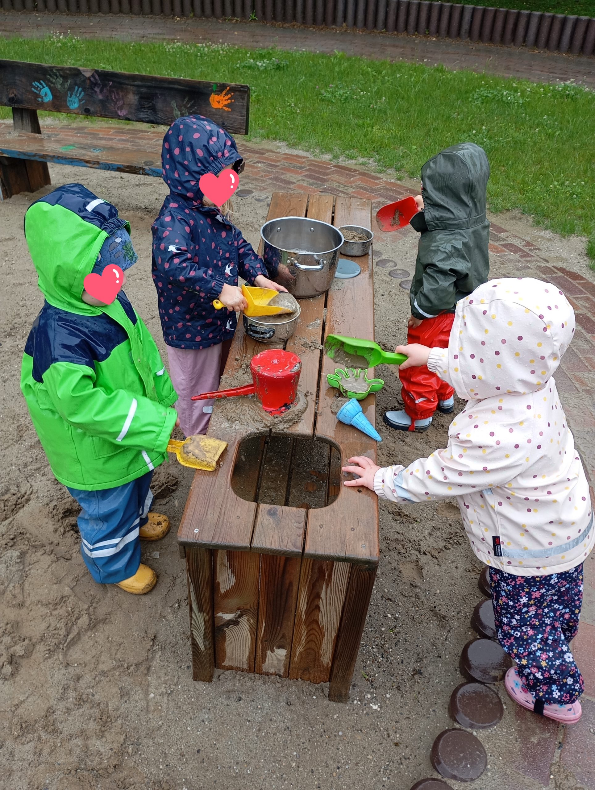 Kinder in Regenkleidung am Matschtisch