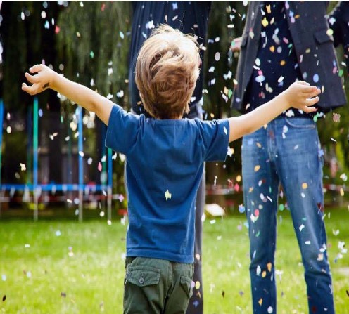 Junge läuft im Rasen. Um ihm rum fliegen Konfetti.
