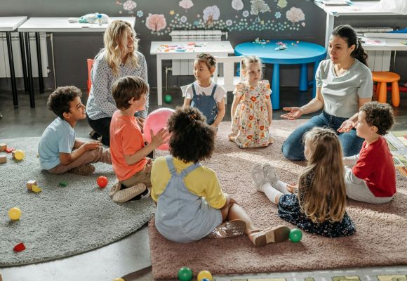 Erzieherinnen und Kinder sitzen im Kreis