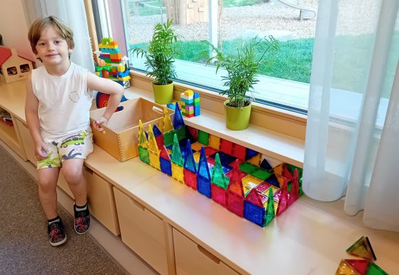 Kind stolz vor selbstgebautem Haus aus Magnetbausteinen